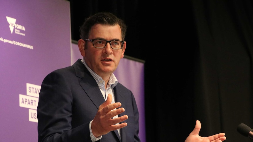 Daniel Andrews in a suit speaks behind a lectern against a purple background.