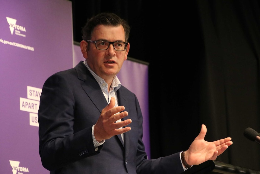 Daniel Andrews in a suit speaks behind a lectern against a purple background.