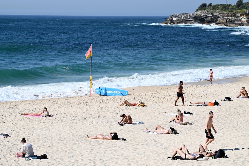 A number of people lay on the sand at Bondi beach.