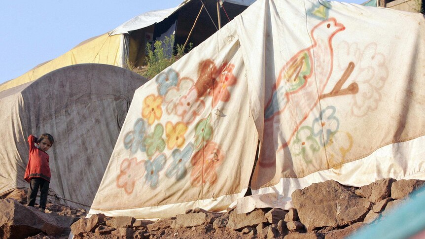 A young Pakistani Kashmiri earthquake survivor stands next to a make-shift tent.