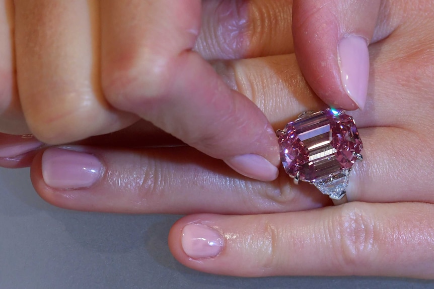 A woman's light pink painte nails are seen tilting the large gem on her finger.