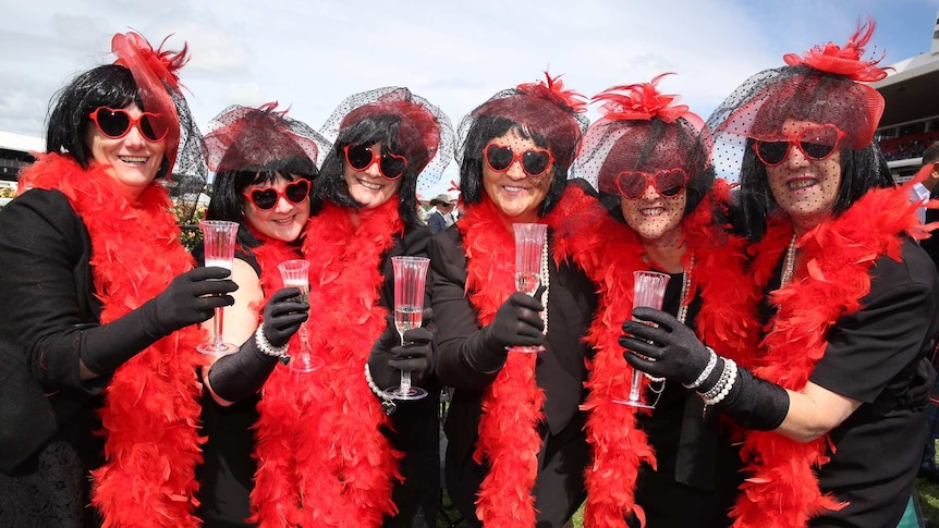 Six friends wearing matching costumes and sunglasses pose for the camera at the Melbourne Cup
