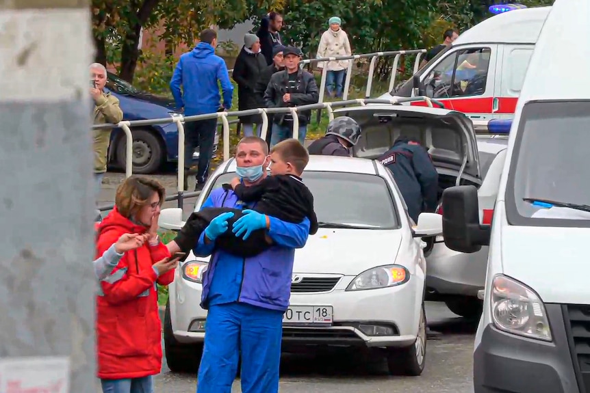 A male emergency worker carries a little boy out of a school.