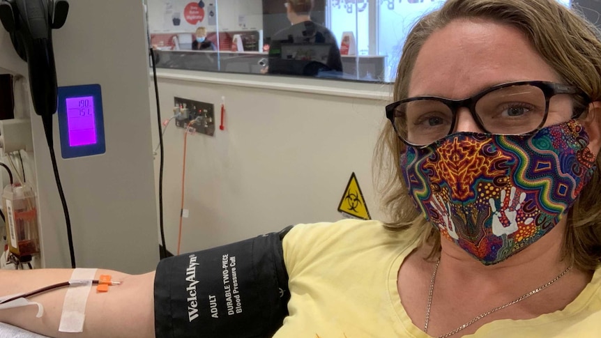 Woman in face mask gives blood at donation centre