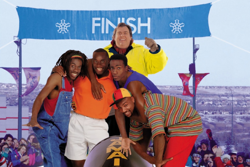 John Candy with four black actors who have their arms around each other and are standing behind a bobsled