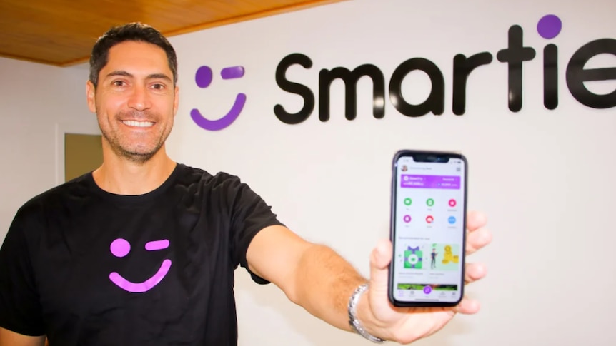 A man holds a phone showing a new app he invented.
