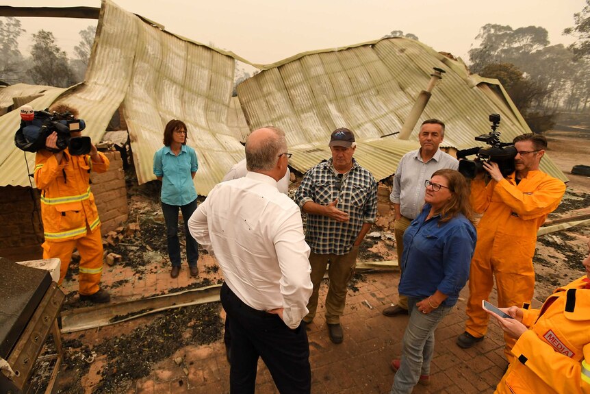 Scott Morrison chats to farmers, surrounded by a burnt out farm and destroyed sheds