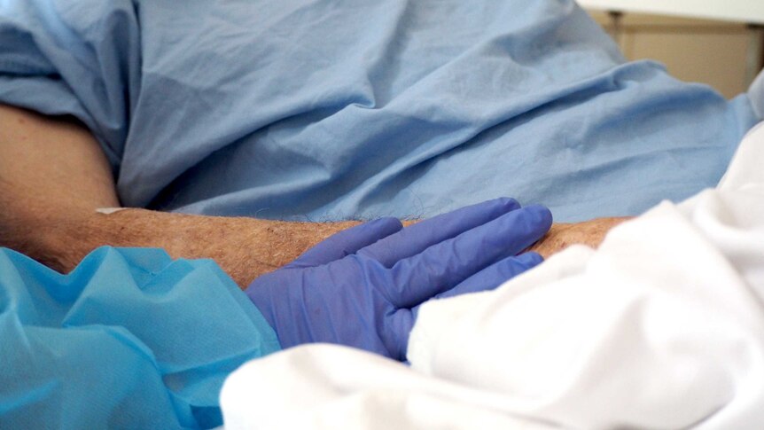 A gloved hand touches a patient's arm in a gesture of support.