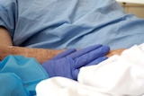 A gloved hand touches a patient's arm in a gesture of support.