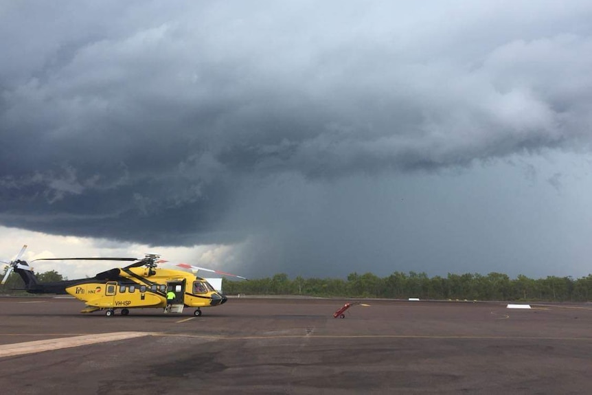 A helicopter sits parked on a airstrip under a stormy sky