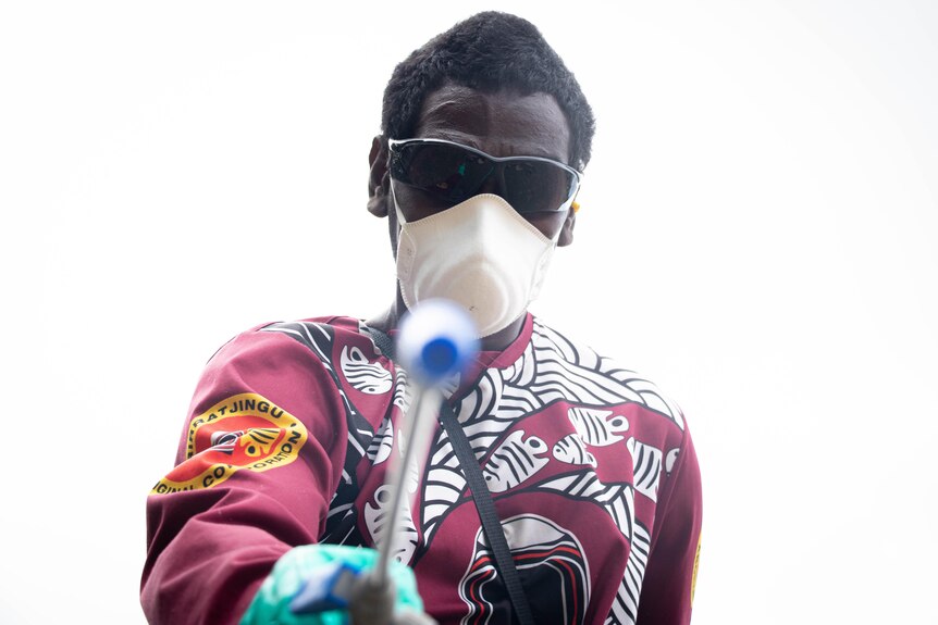 A man wears a mask and sunglasses and sprays chemicals
