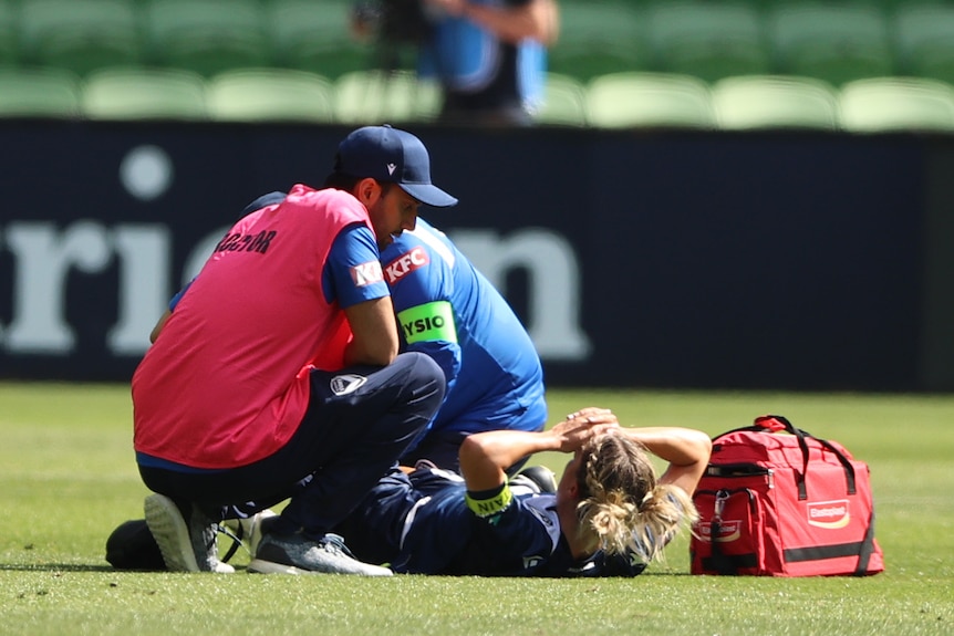 A soccer player lays on her back and receives treatment from a doctor after an injury