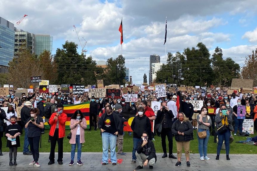 Protesters stand holding placards, most wearing face masks