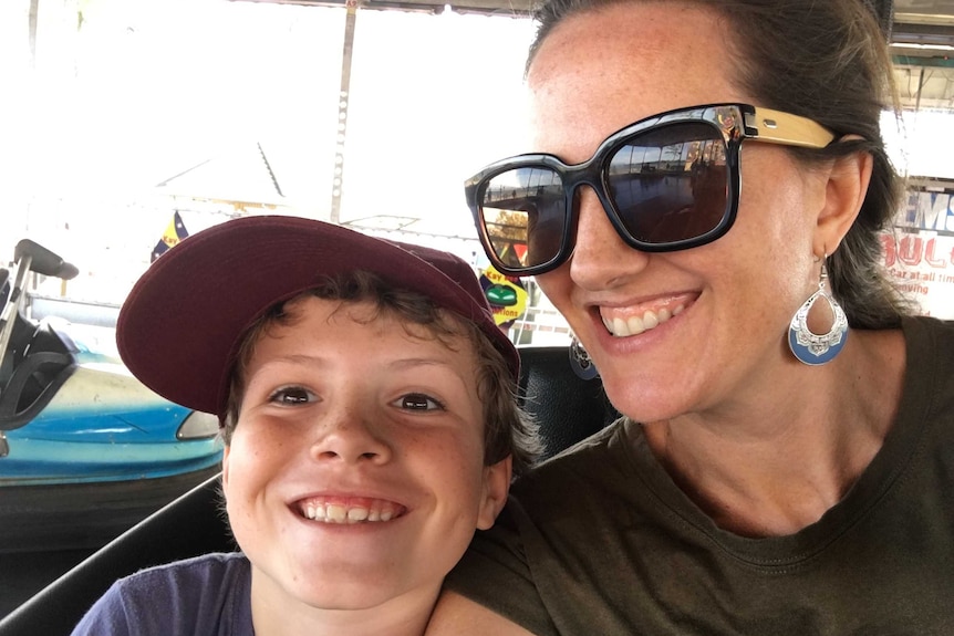 A young boy smiling next his mum who is also smiling and wearing large sunglasses