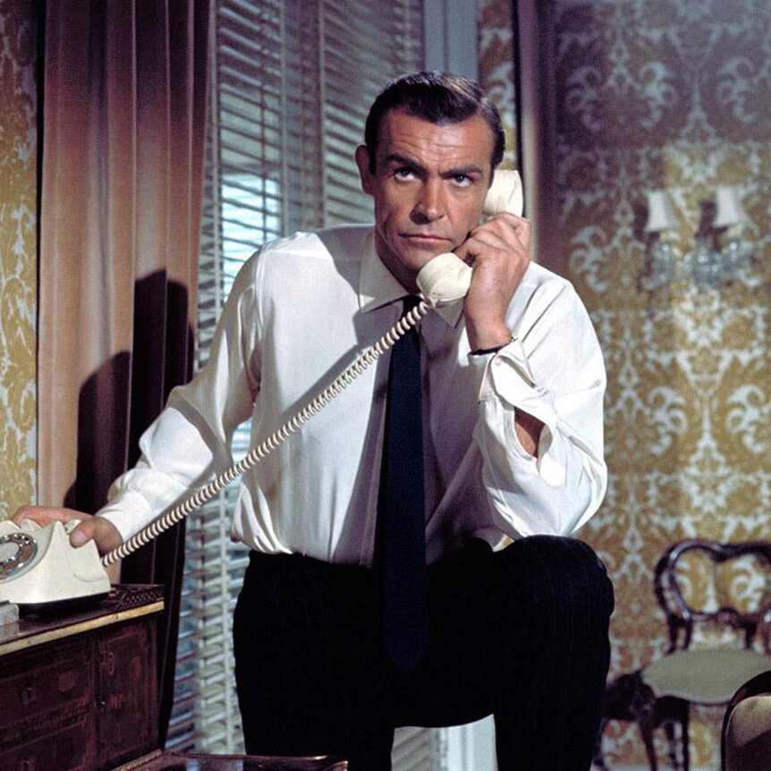 Sean Connery as James Bond, speaking on an old dial telephone with a furrowed brow.