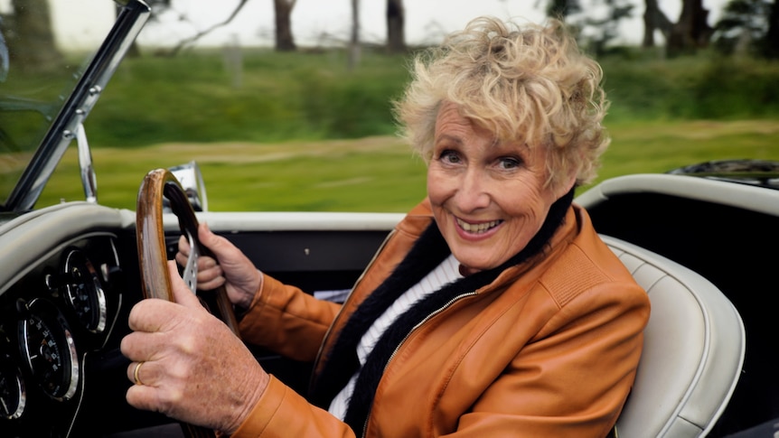 Woman smiling wearing a leather jacket driving an open top vehicle