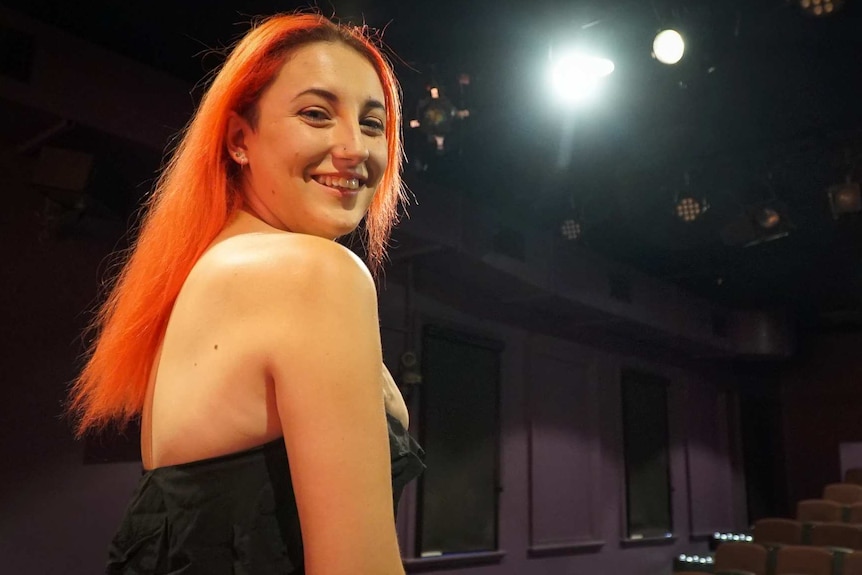 A woman with red hair stands on a theatre stage