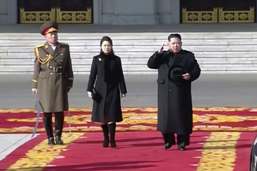 Kim Jong-un along with his wife walks on red carpet inspecting honour guards.