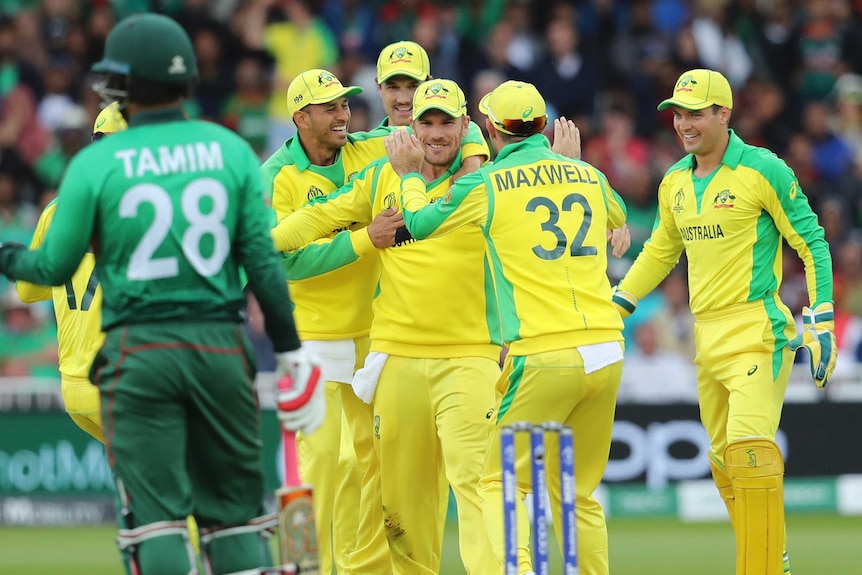 A smiling Aaron Finch is congratulated by his teammates as a Bangladesh batsman looks on in the foreground