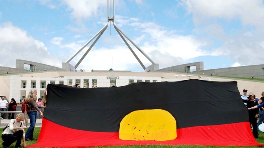 A group of supporters hold a very large aboriginal flag up in the grounds before the Australian Parliament in Canberra.
