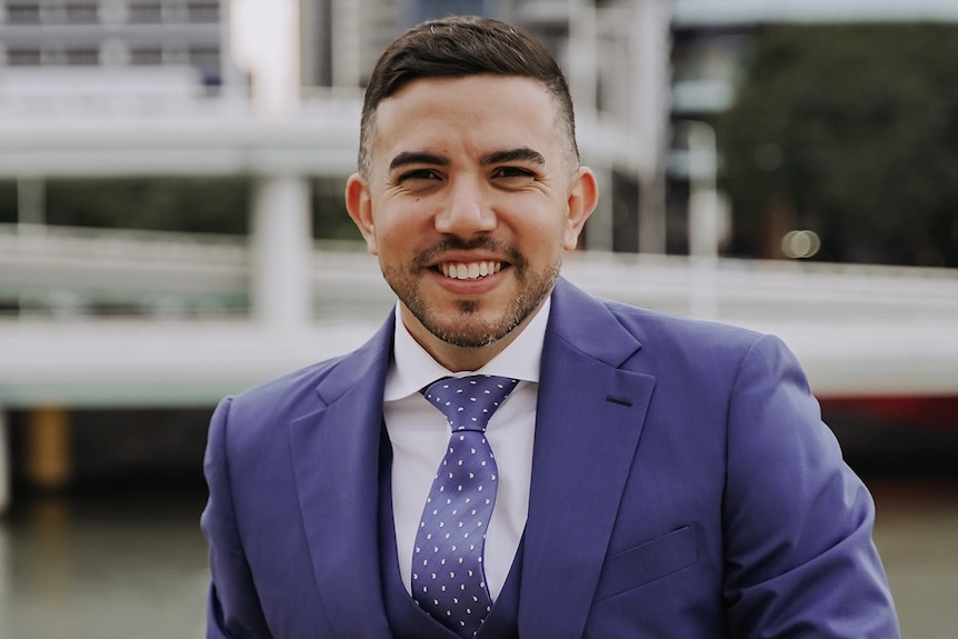 Pedro Marin Ramirez smiles as he stands outside with Brisbane city behind him.