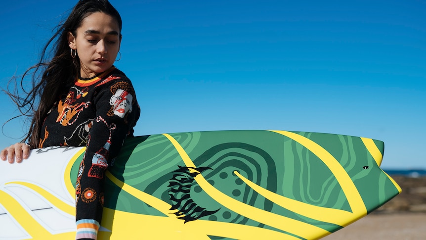 Woman holding a surfboard with indigenous designs