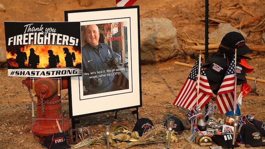 A makeshift memorial has a photo of a firefighter, caps, American flags, solar lights and a hydren