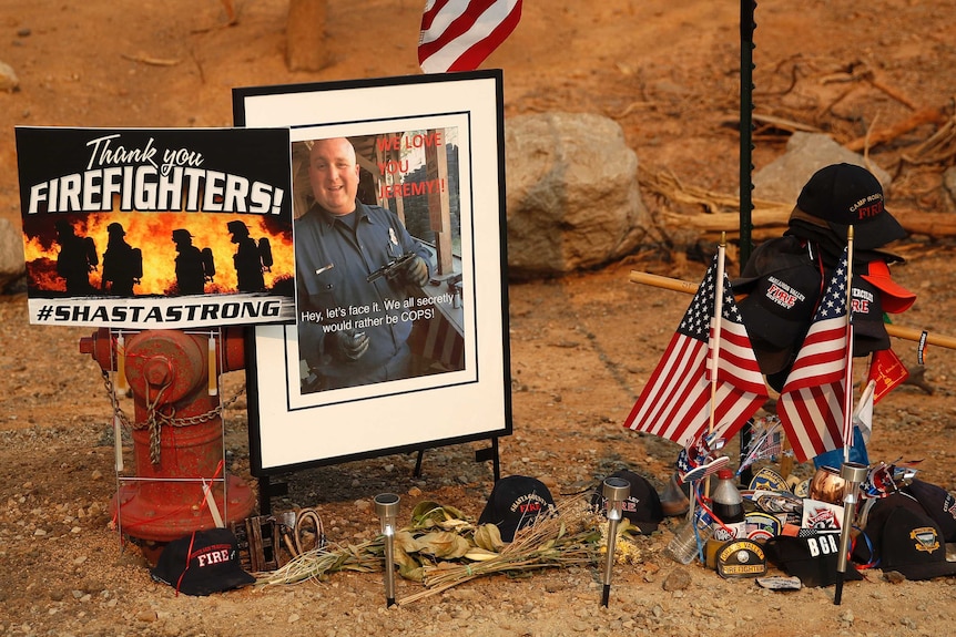 A makeshift memorial has a photo of a firefighter, caps, American flags, solar lights and a hydren