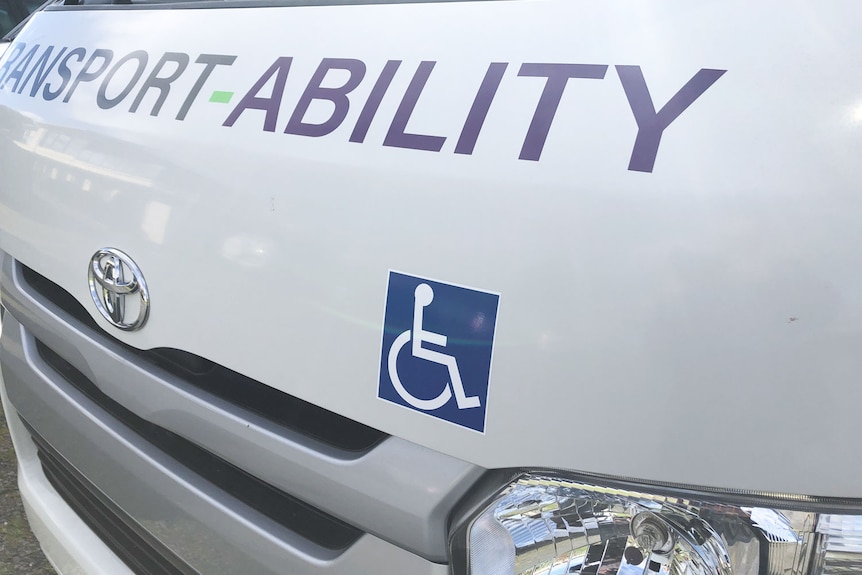 The front of a white van with a disabled logo and the words Transport Ability painted under windscreen