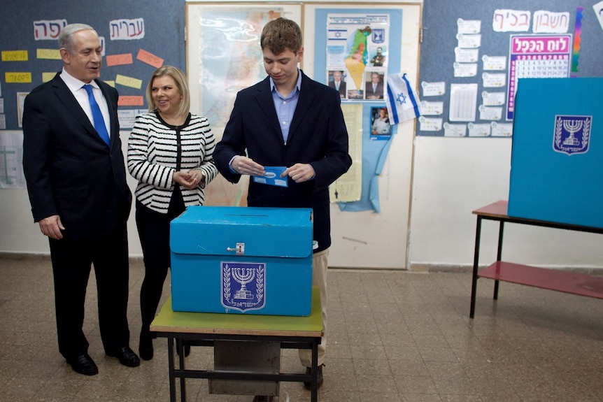 一名年轻男子准备将选票放入盒子中，而一名年长男子和一名女子在一旁观看