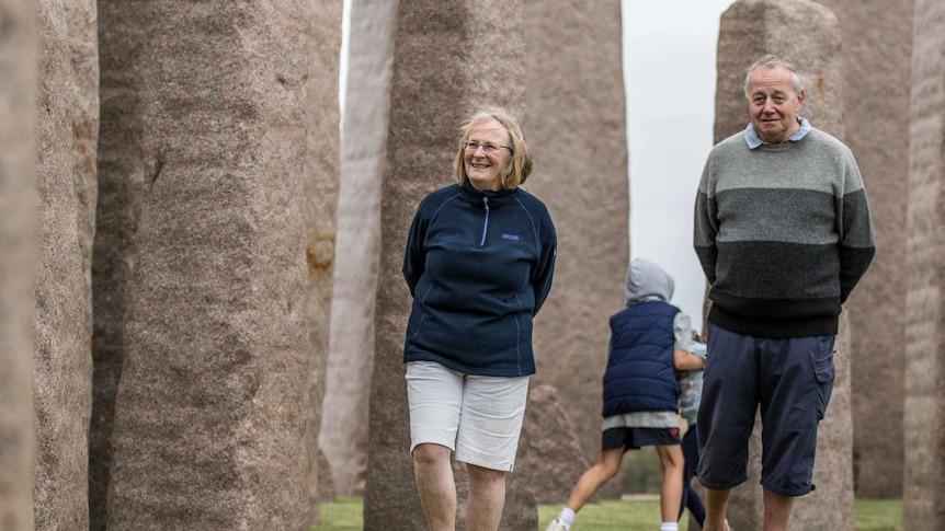 A man and woman walking near a Stonehenge replica.