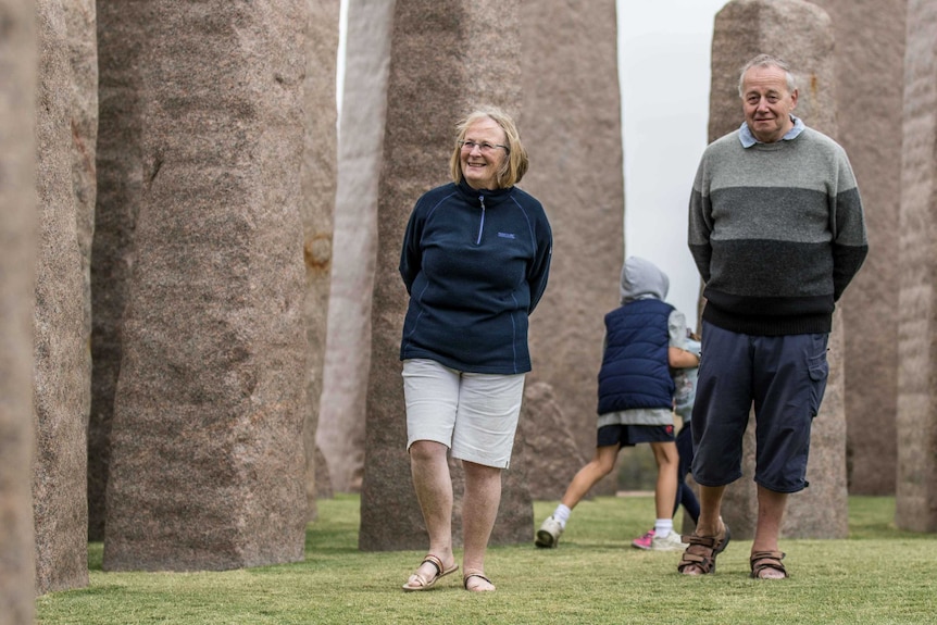 A man and woman walking near a Stonehenge replica.