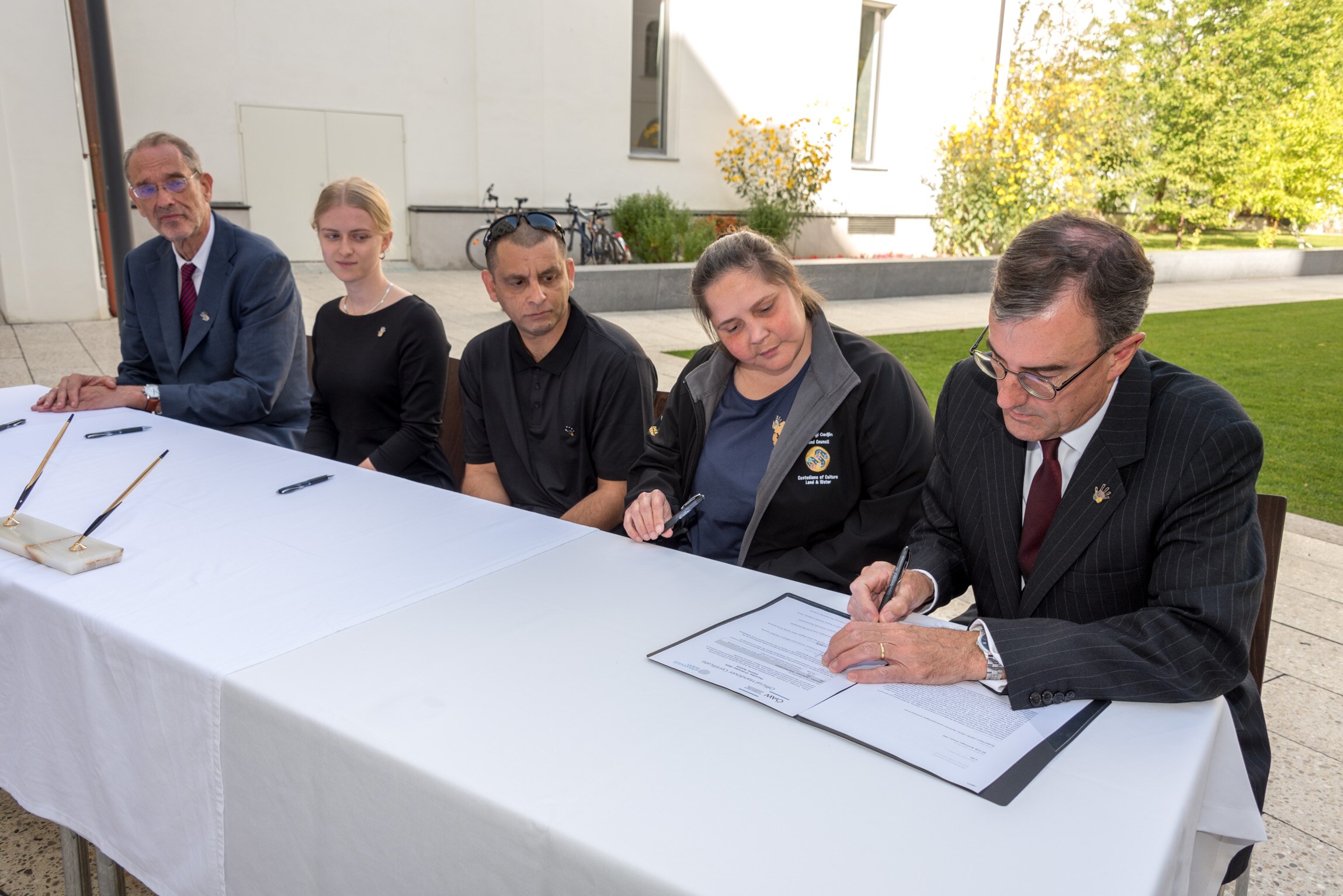 a man signs a document, with Indigenous Australians watching on