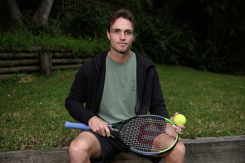 A male tennis player holds a tennis racquet as he poses for a photo in Sydney.