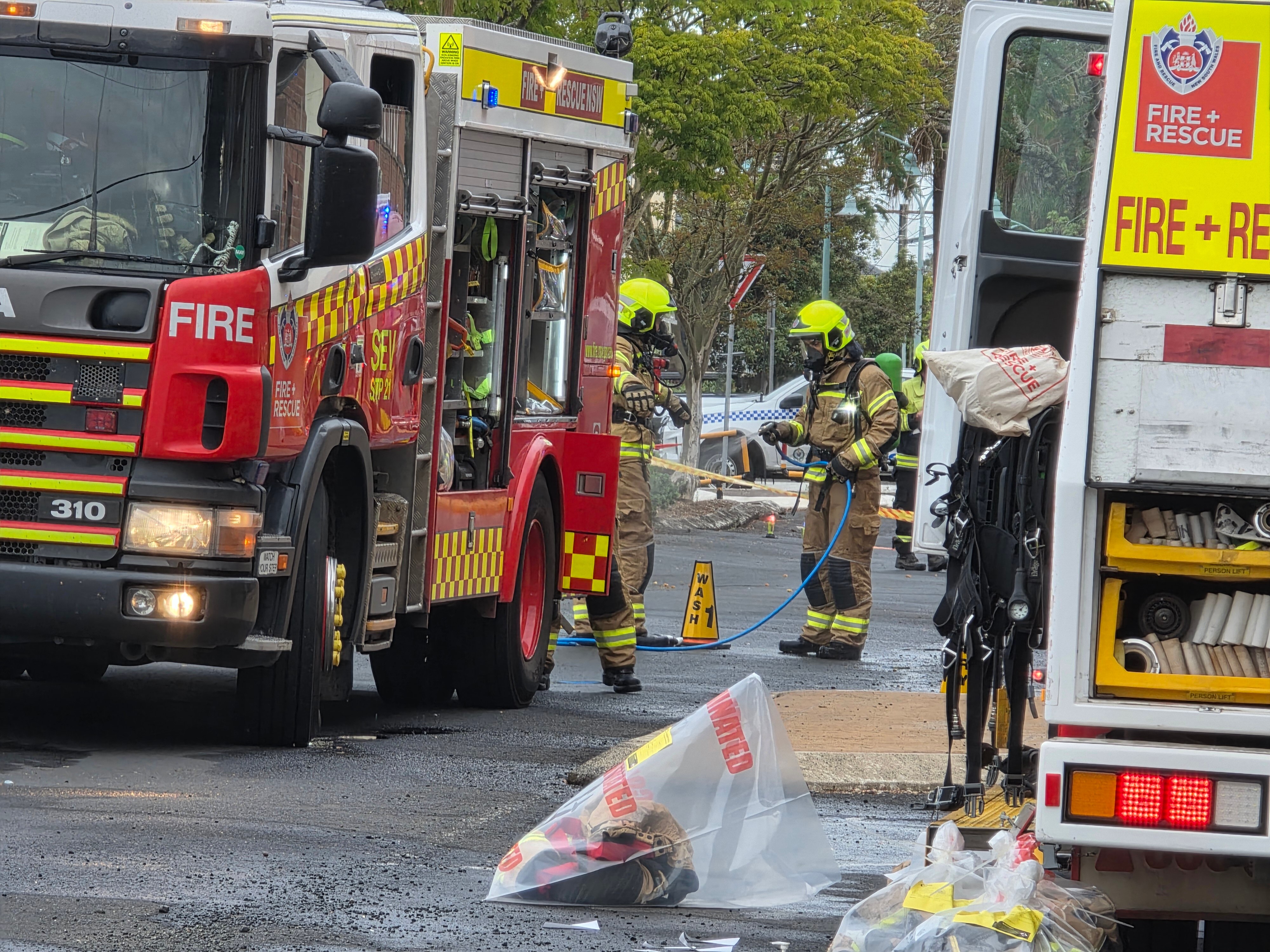 Deux pompiers tiennent des lances à incendie alors qu'ils se tiennent à côté de camions de pompiers à l'extérieur du Lismore Masonic Hall
