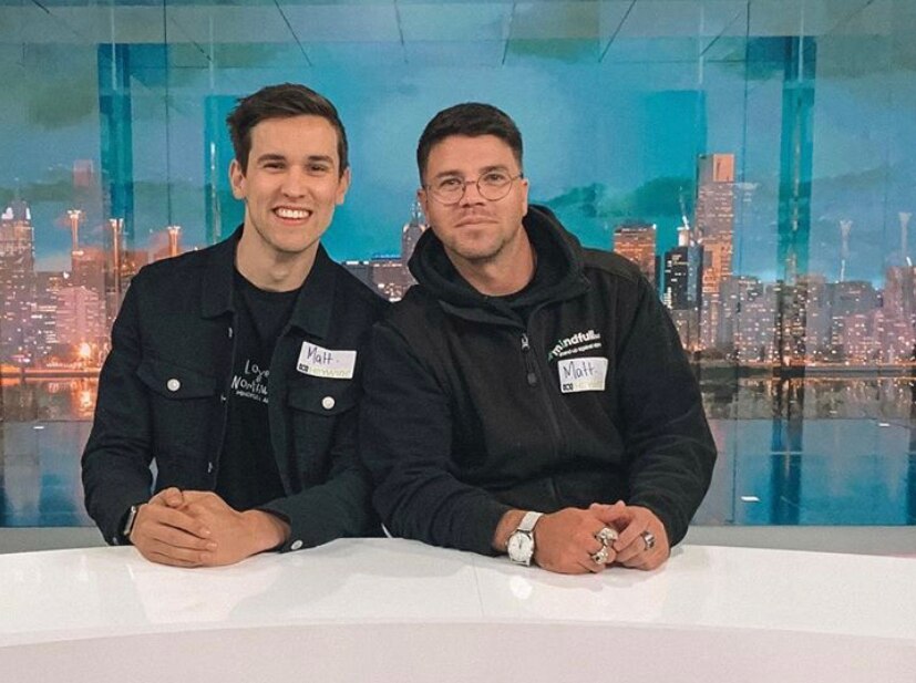 Matthew Searle sits on the left wearing a dark jacket sat next to Matthew Runnalls. They are in front of a city backdrop.