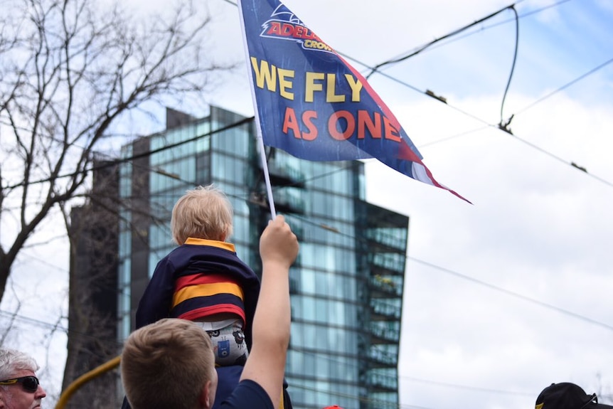 An Adelaide fan with a toddler on his shoulders, waving a Crows flag.