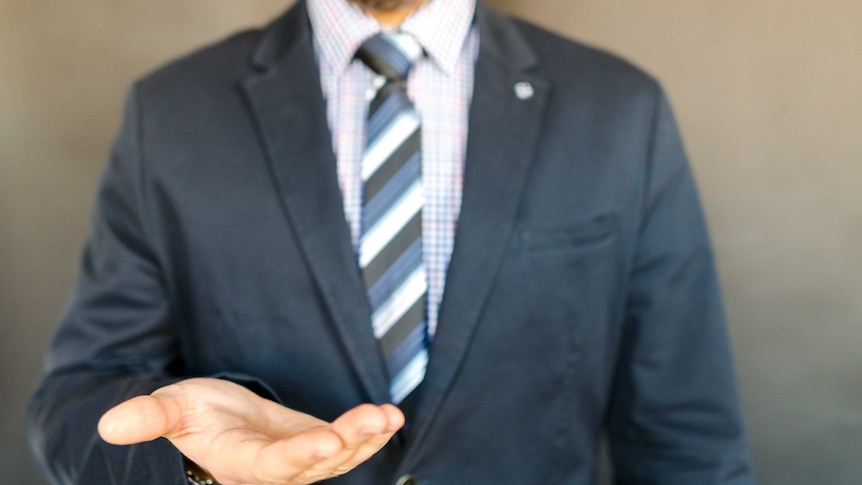 A man in a suit holds out his hand.