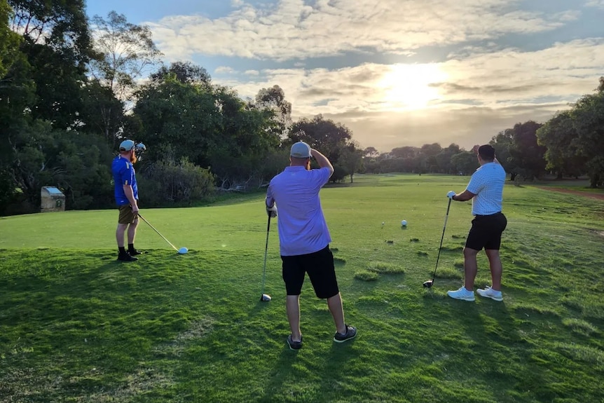 A picture of three men playing golf with the fairway in the background and the sun behind the clouds
