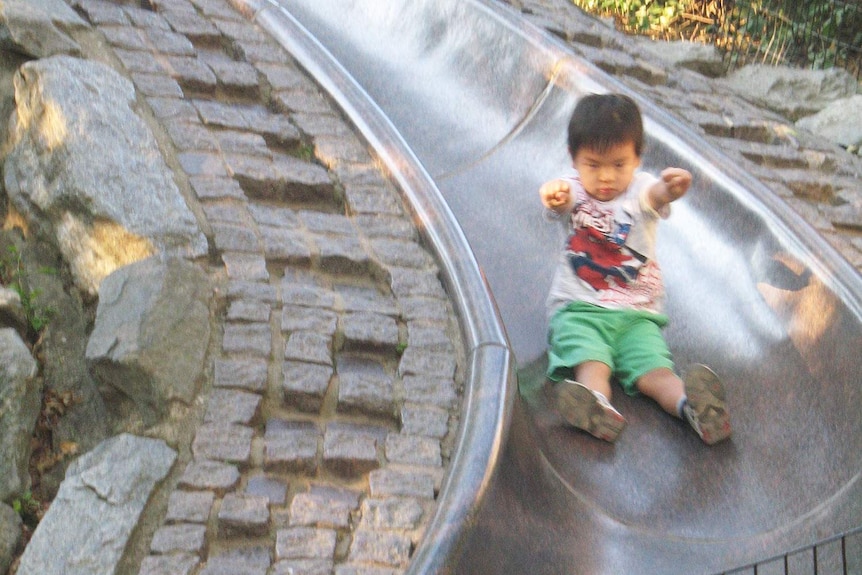 Small boy rides slippery dip with arms raised like Superman