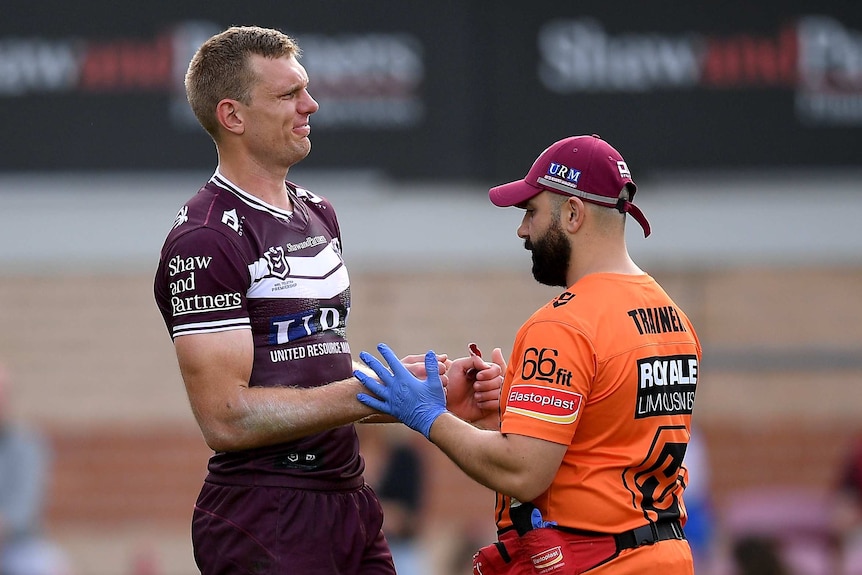 A Manly Sea Eagles NRL receives treatment from a trainer during the match against the Gold Coast Titans.