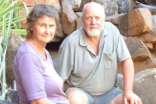 An older man and woman sitting on rocks posing for a photograph.