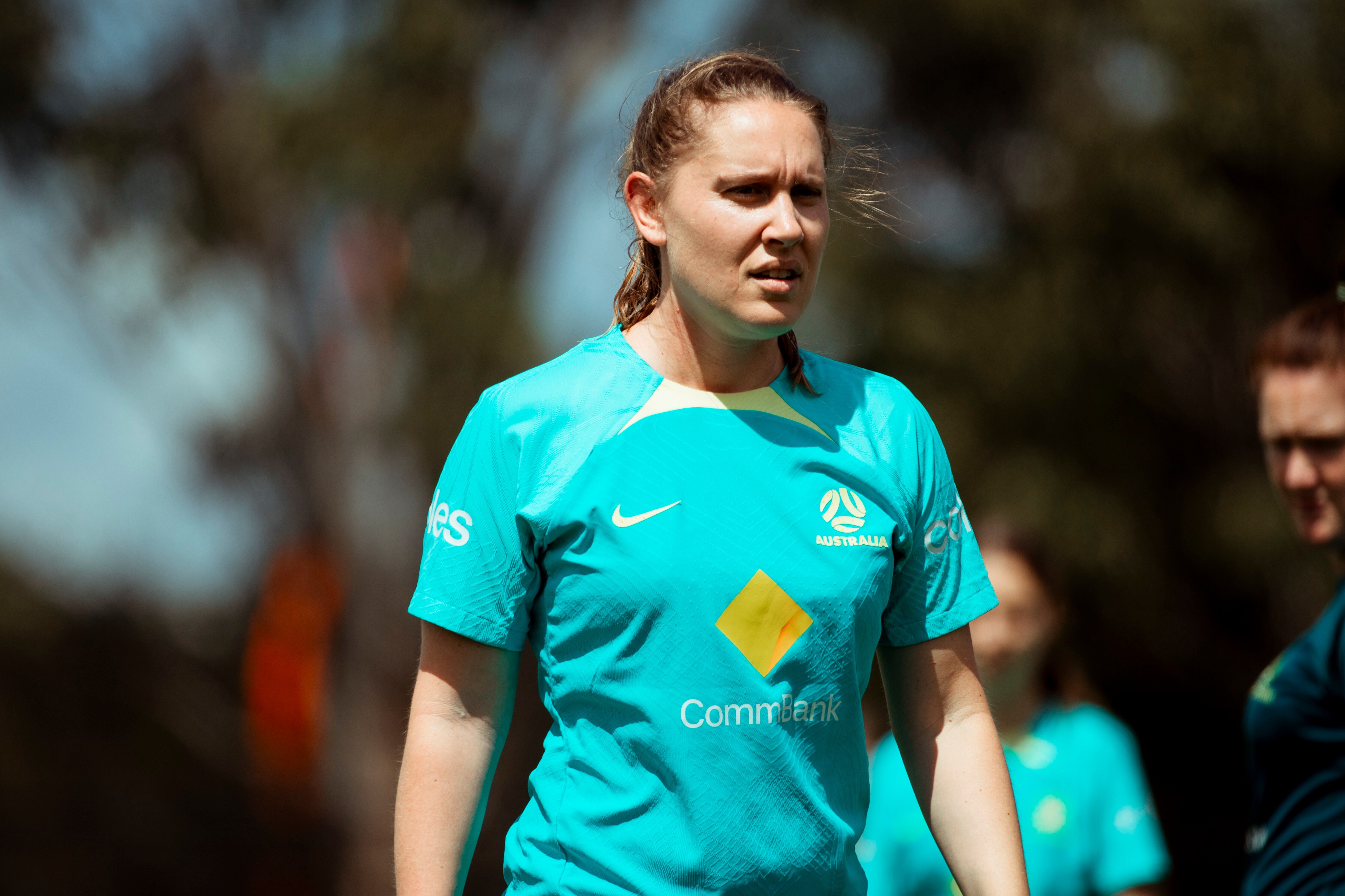 A female soccer player wearing a turquoise training shirt and long, tied-up hair looks off centre .