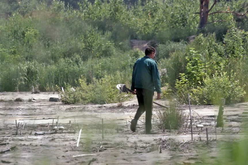 A man walks through an area stripped by mining holding a shovel.