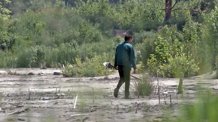 A man walks through an area stripped by mining holding a shovel.