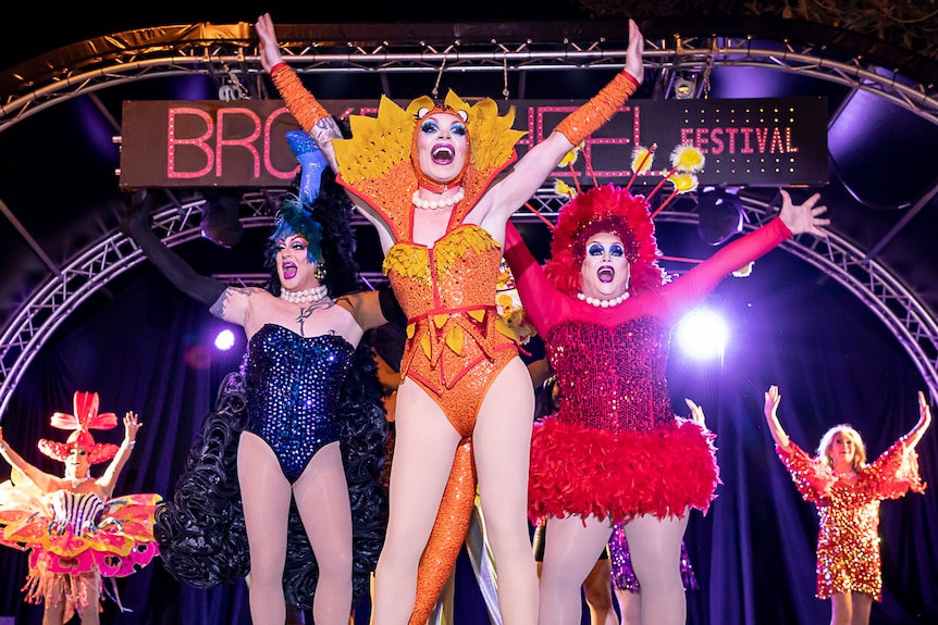 Three drag queens wearing colourful outfits dance up a storm on stage.