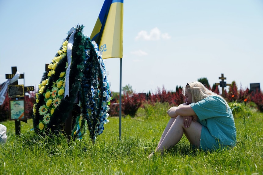 A woman woman who is upset, sitting on some grass near a grave