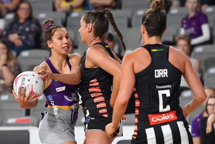 A Queensland Firebirds Super Netball player holds the ball to her right while being defended by a Magpies player.
