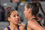 A Queensland Firebirds Super Netball player holds the ball to her right while being defended by a Magpies player.