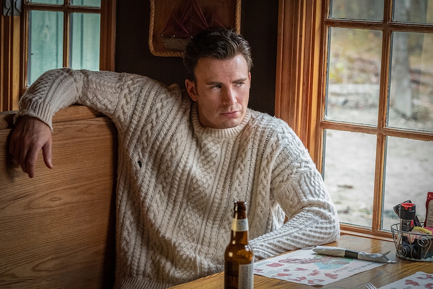 Chris Evans wears off white knitted jumper and sits next to window in wooden diner booth with beer and table setting.